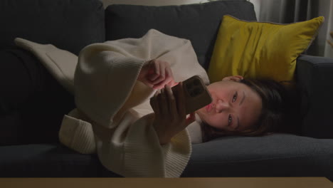 Woman-Spending-Evening-At-Home-Lying-On-Sofa-With-Mobile-Phone-Scrolling-Through-Internet-Or-Social-Media-10